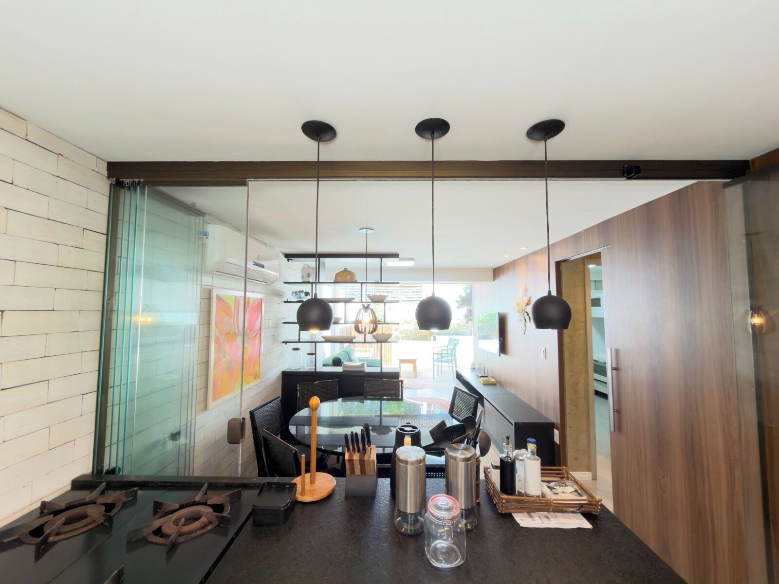 A modern kitchen with a dining area, featuring a black countertop, hanging pendant lights, and a view into the dining room.