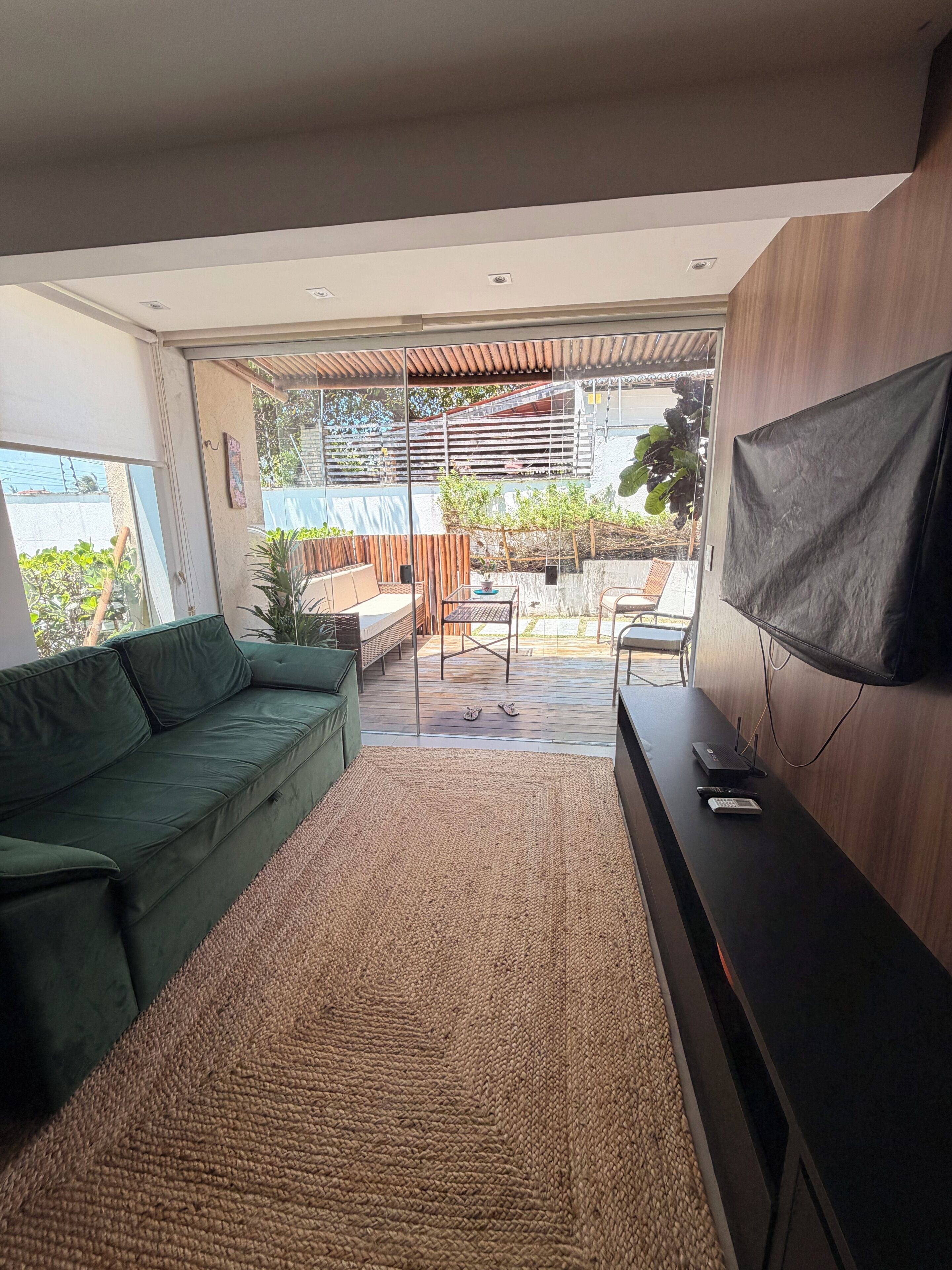 Un salon moderne avec un canapé vert, un téléviseur à écran plat fixé au mur et une vue sur la terrasse extérieure.