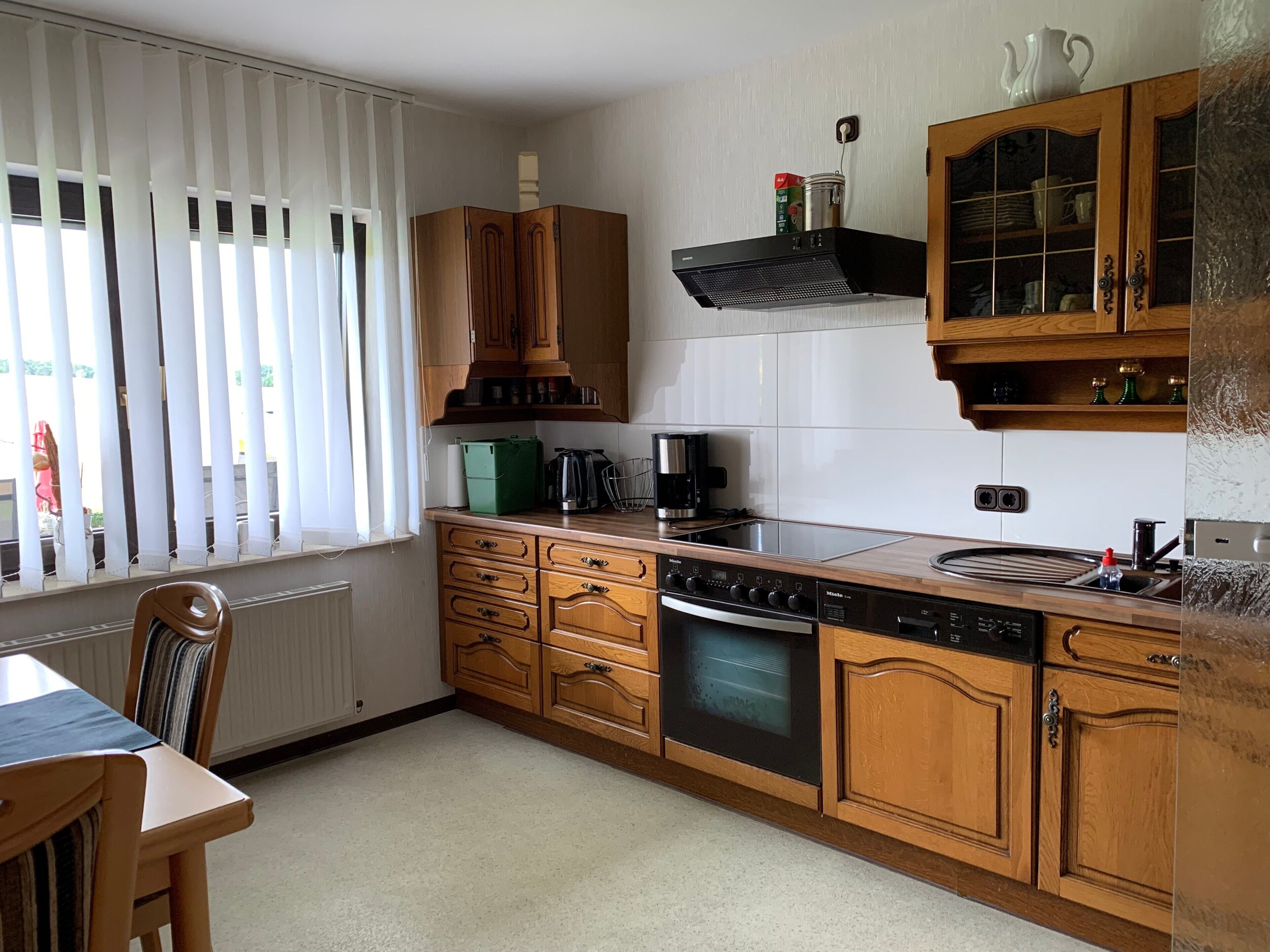 A kitchen with wooden cabinets, a stove, a sink, and a window with blinds.