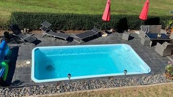 Ein rechteckiger Swimmingpool mit einer gefliesten Liegefläche, umgeben von Liegestühlen und einem roten Sonnenschirm.