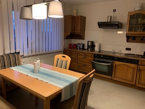 A kitchen with wooden cabinets, a dining table with a striped tablecloth, and a window with vertical blinds.