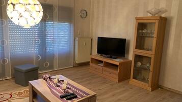 A living room with a wooden TV stand, a glass cabinet, a table with remote controls, and a decorative light fixture.