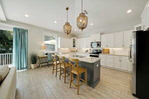 A modern kitchen with white cabinets, a large island with bar stools, a black refrigerator, and two hanging crystal chandeliers. - Silver Surf- A stunning family home 2 blocks from the beach. (Holmes Beach)
