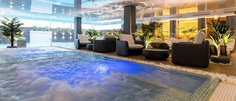 A heated indoor pool area with seating and plants.