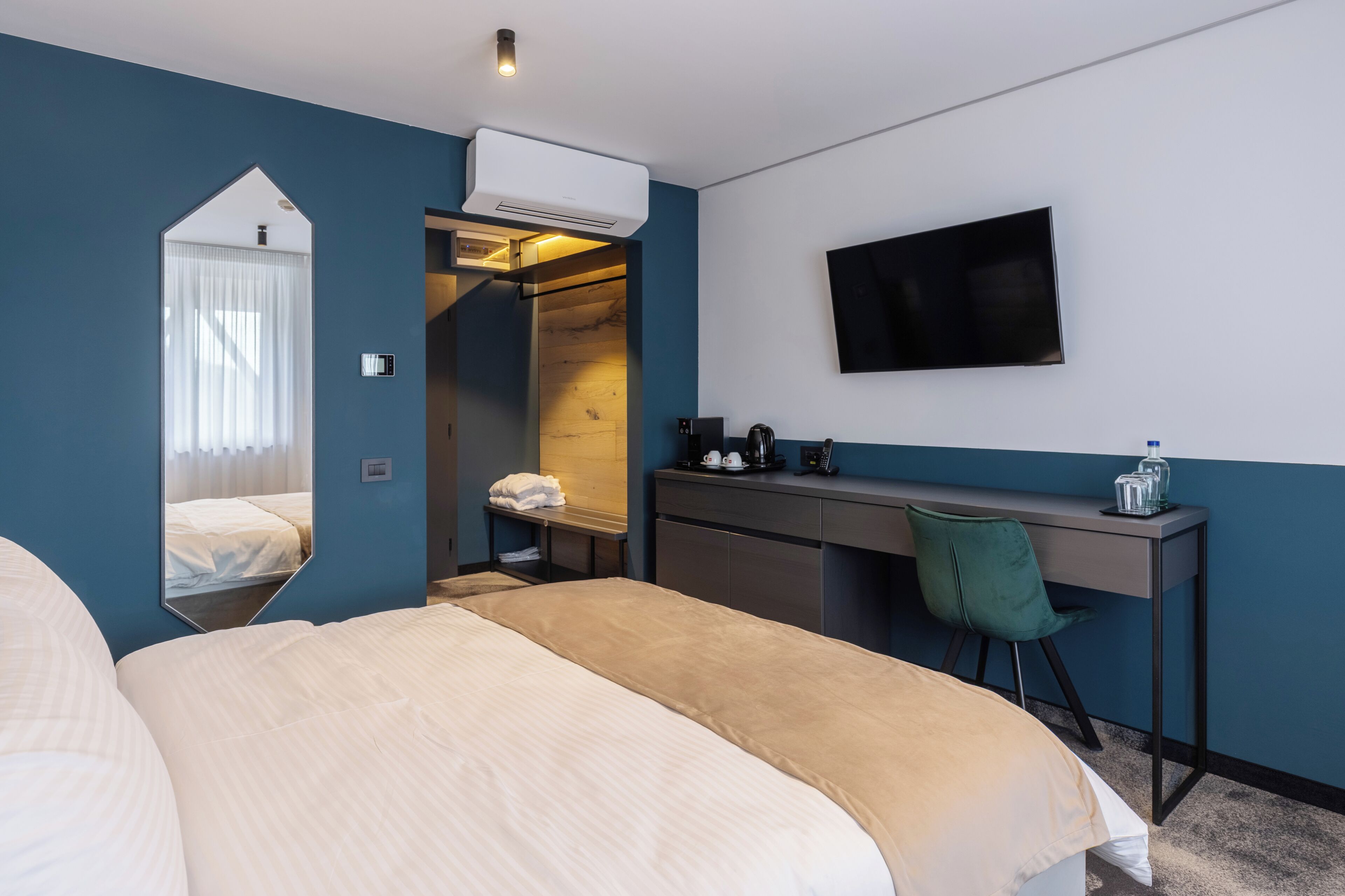 A hotel room with a bed, a desk, a chair, a TV, and an air conditioning unit.