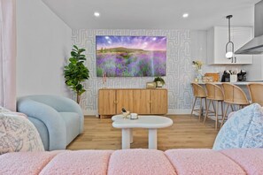 A modern living room with a sofa, a coffee table, a TV mounted on the wall, and a kitchen area with bar stools. - Pixel Palace•Spa•Gameroom•Theatre•Sleeps 14 (San Diego)