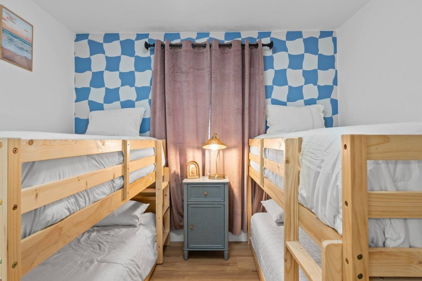 Una habitación con dos literas, una mesita de noche pequeña con una lámpara y un patrón de pared a cuadros.