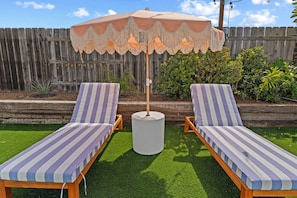 Two lounge chairs with striped cushions, a decorative umbrella, and a wooden fence in the background. - Pixel Palace•Spa•Gameroom•Theatre•Sleeps 14 (San Diego)