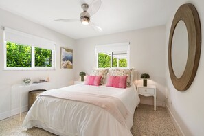 Une chambre à coucher comprenant un lit, des tables de chevet, un miroir et des fenêtres donnant sur un paysage verdoyant.