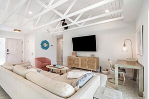 A modern living room with a white sofa, a pink armchair, a coffee table, a television mounted on the wall, and a small desk with a lamp. - St Pete Beach Vina Del Mar Waterfront Pool (St Pete Beach)