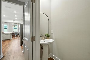 Ein Flur, der zu einer Küche und einem Badezimmer mit einem weißen Waschbecken und einer Pflanze führt.