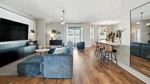 A modern living room with a large flat-screen TV, a sofa set, a dining area with bar stools, and a kitchen visible through an open door. - Casa Azul at the Cape - a family friendly 5-bedroom paradise! (Cape Coral)