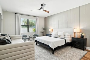 Ein modernes Schlafzimmer mit Bett, Nachttischen, Schreibtisch, Stuhl und Deckenventilator.