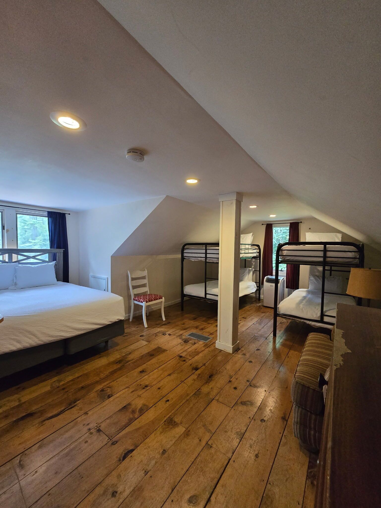 A room with a bunk bed, a single bed, a chair, and a window.