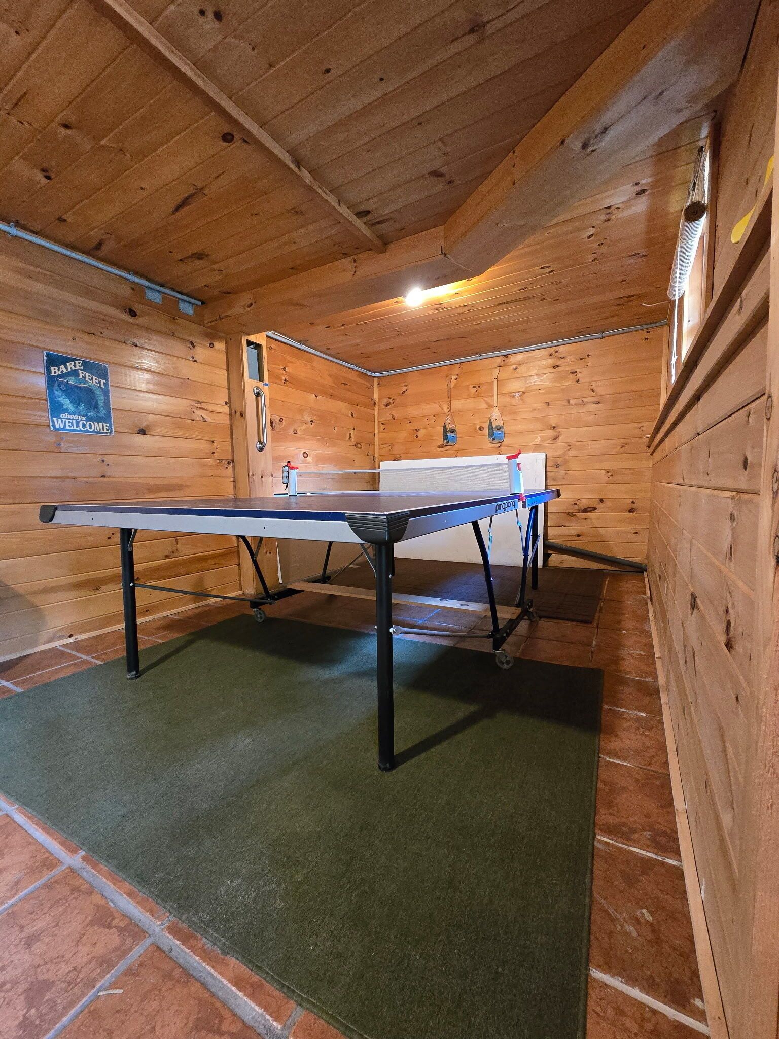 Une table de ping-pong dans une pièce en bois, avec un panneau accroché au mur.