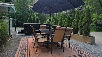 Une terrasse extérieure avec une table et des chaises, un grand parasol et un tapis décoratif.