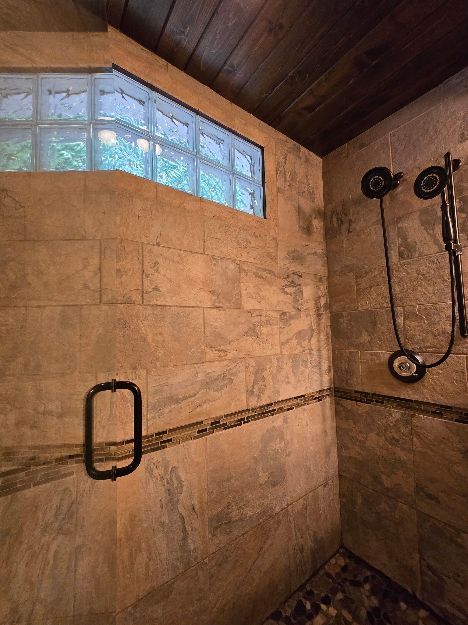 A stone-walled shower with a window above, a handheld showerhead, and a handheld shower attachment.