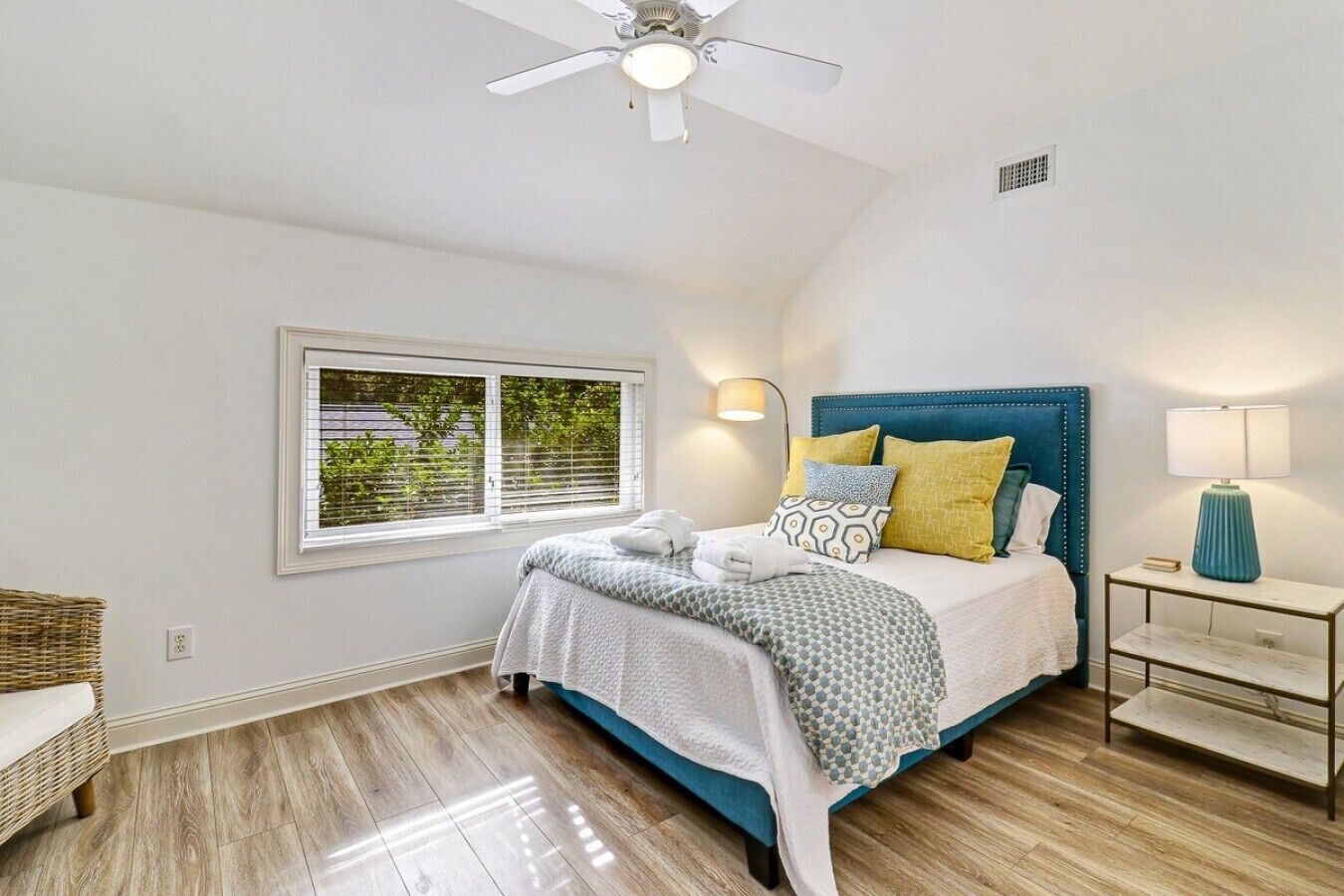 Une chambre à coucher avec un lit, un ventilateur de plafond, une table de chevet avec une lampe et une fenêtre avec des stores.
