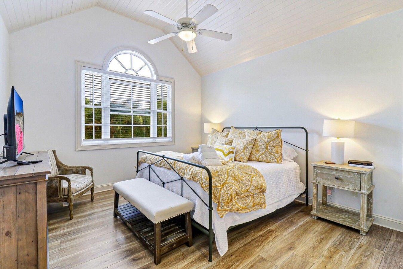 A bedroom with a bed, a desk, a chair, a bench, a nightstand, and a window with blinds.