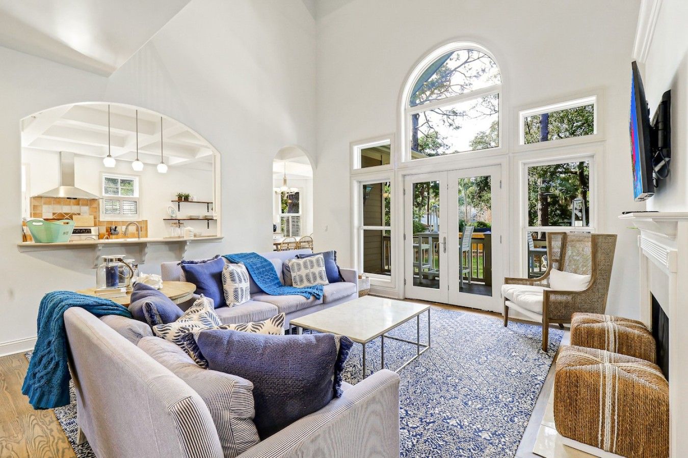 A spacious living room with a large sofa, a coffee table, and a fireplace. There are arched windows and a kitchen visible in the background.