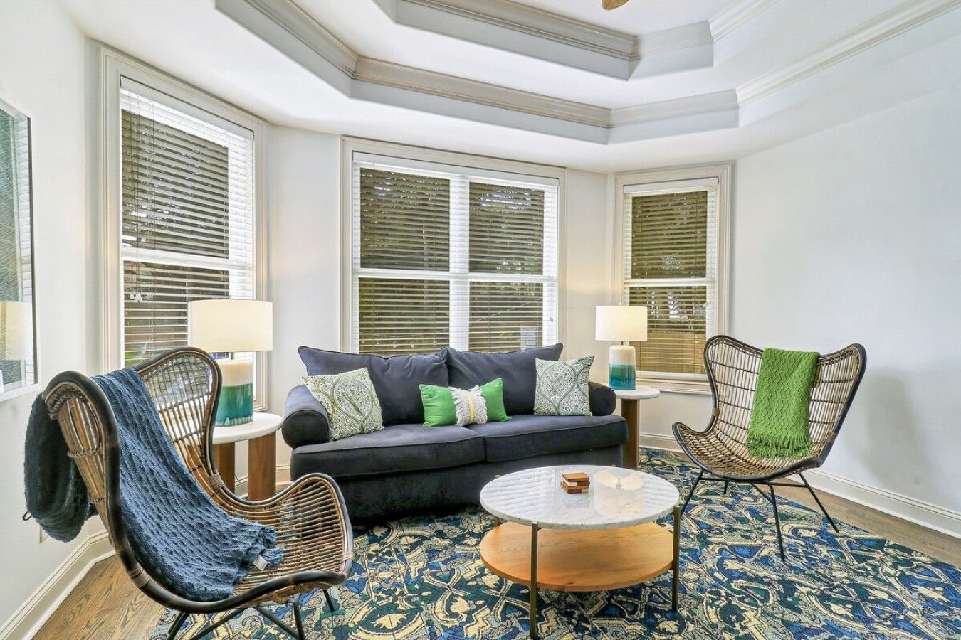 A room with a dark-colored sofa, two wicker chairs, a small round table, and patterned carpet.