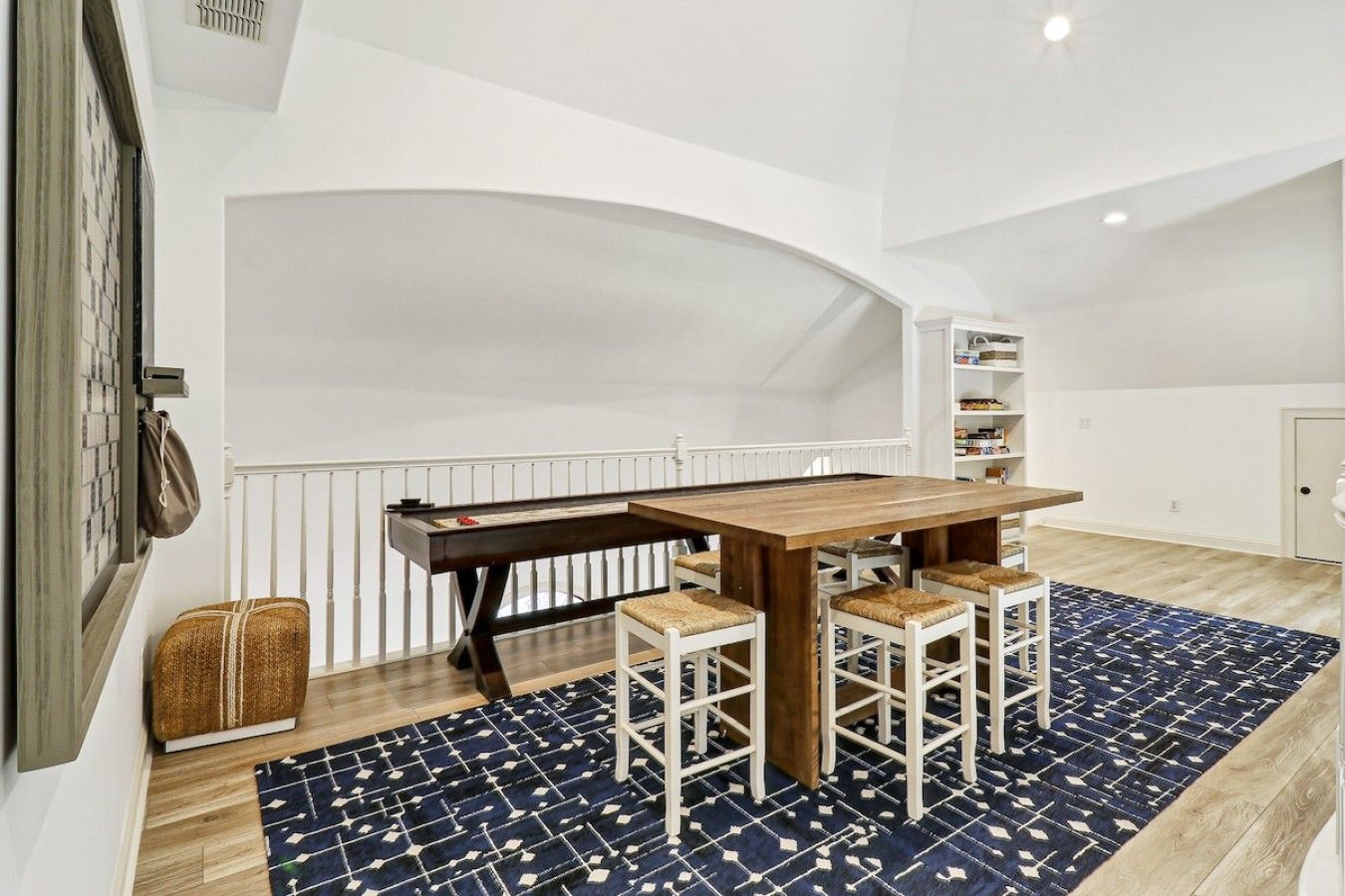 A dining area with a wooden table and four chairs, a patterned rug, and a white railing.