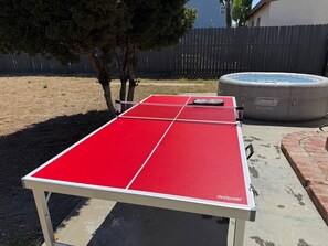 Ein roter Tischtennis-Tisch mit Netz, draußen gelegen, mit einem Holzzaun und Bäumen im Hintergrund.