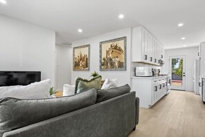 A modern living room with a grey sofa, a flat-screen TV, and two framed historical photographs on the wall. - The 90s Clubhouse: Hot Tub + Games + Fam Friendly (San Diego)