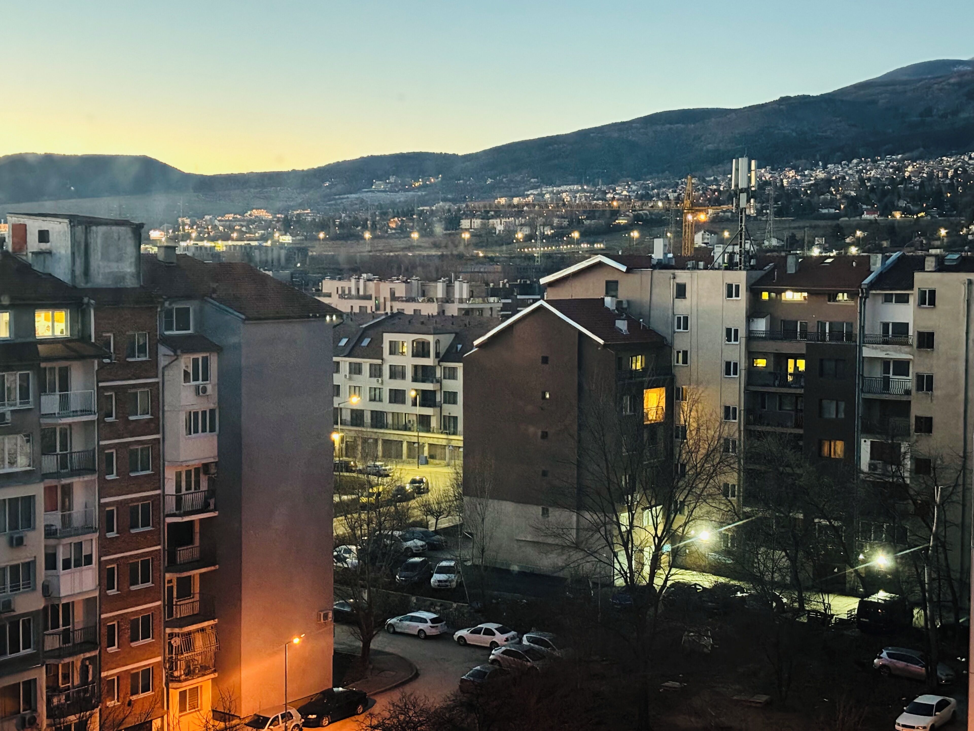 Un quartier résidentiel composé d’immeubles à plusieurs étages, d’un parking et offrant une vue lointaine sur une ville et un pont.