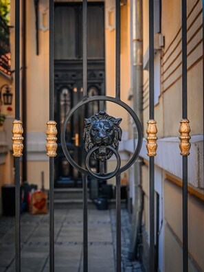 Un estrecho callejón con una verja metálica que presenta un escudo con cabeza de león.