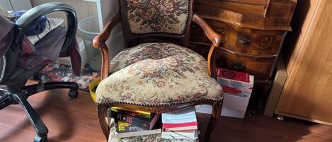 A vintage-style chair with floral upholstery, a wooden desk with various items, and a wooden cabinet with drawers.
