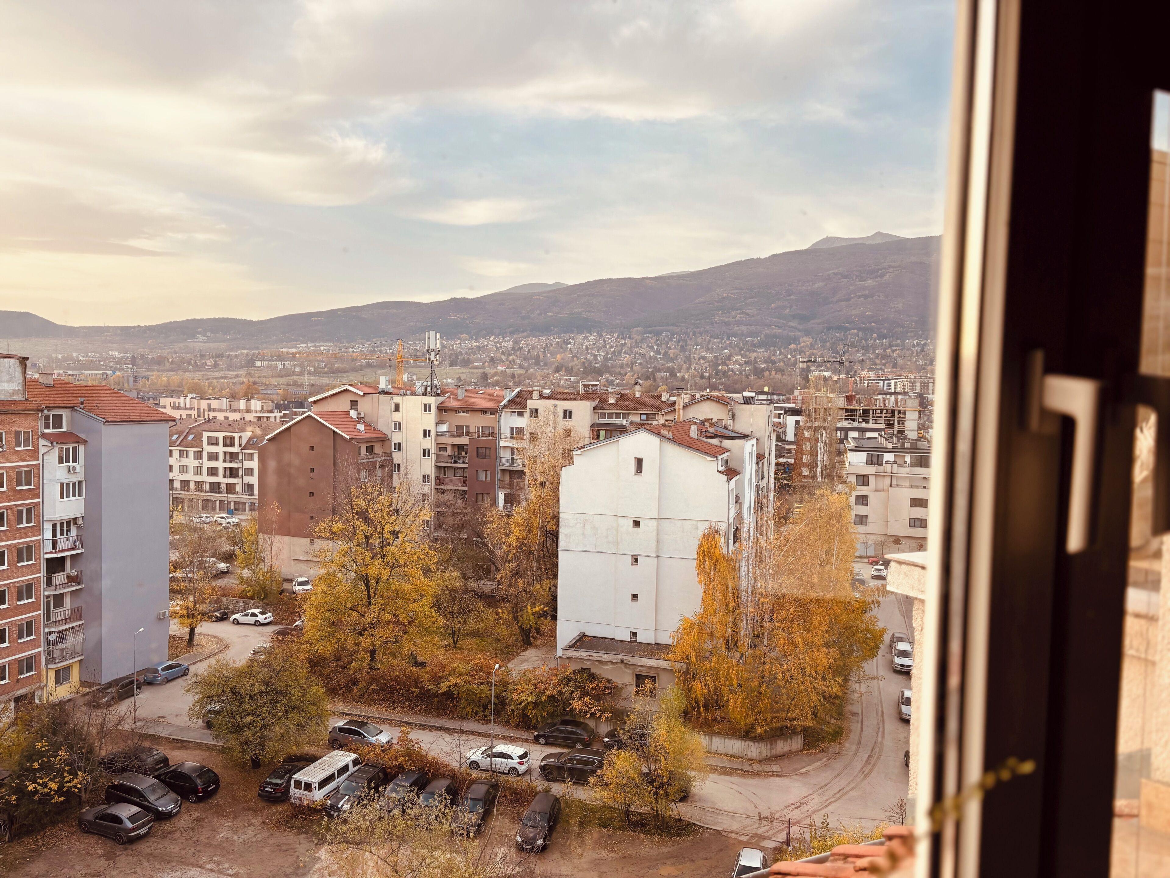 A residential area with multi-story buildings, a parking lot, and autumn foliage.