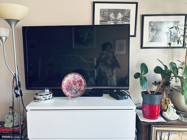 A television on a white stand with a decorative plate, a lamp, and a potted plant.