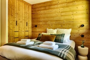 Ein Schlafzimmer mit hölzernem Kopfteil, einem Bett mit vielen Kissen und einer Decke sowie einem Nachttisch mit einer Vase.