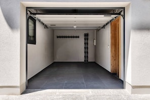 Eine Garage mit geschlossenem Garagentor, Fliesenboden und einer Holztür rechts.