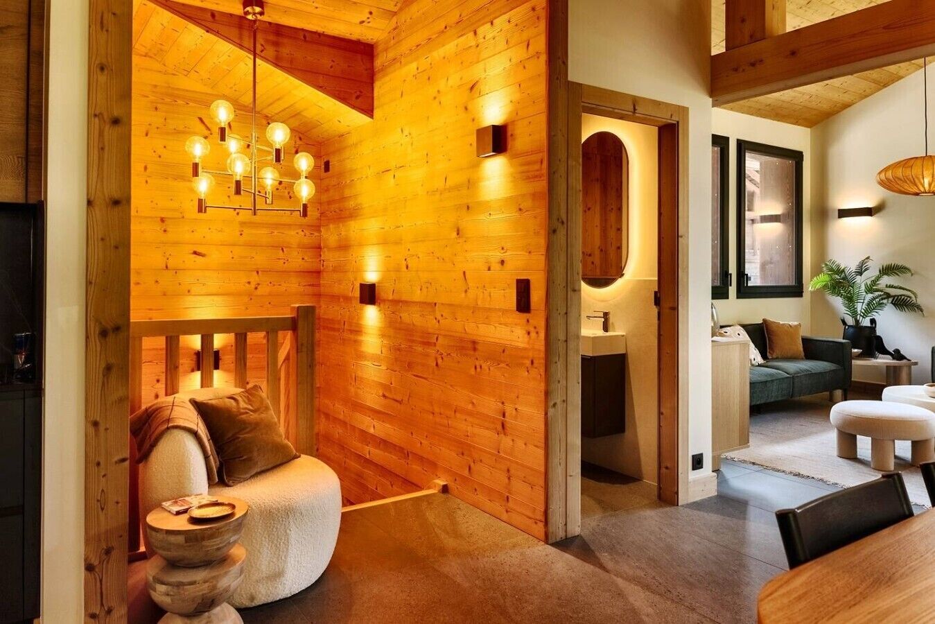 A cozy interior with a wooden wall, a modern light fixture, a sofa, a dining table, and a plant.
