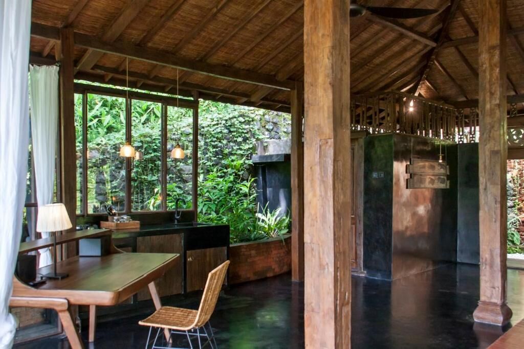 A wooden interior with a dining area, a fireplace, and a view of greenery outside.
