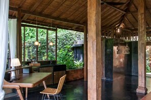 A wooden interior with a dining area, a fireplace, and a view of greenery outside. - Villa Mahadevi (Gianyar)