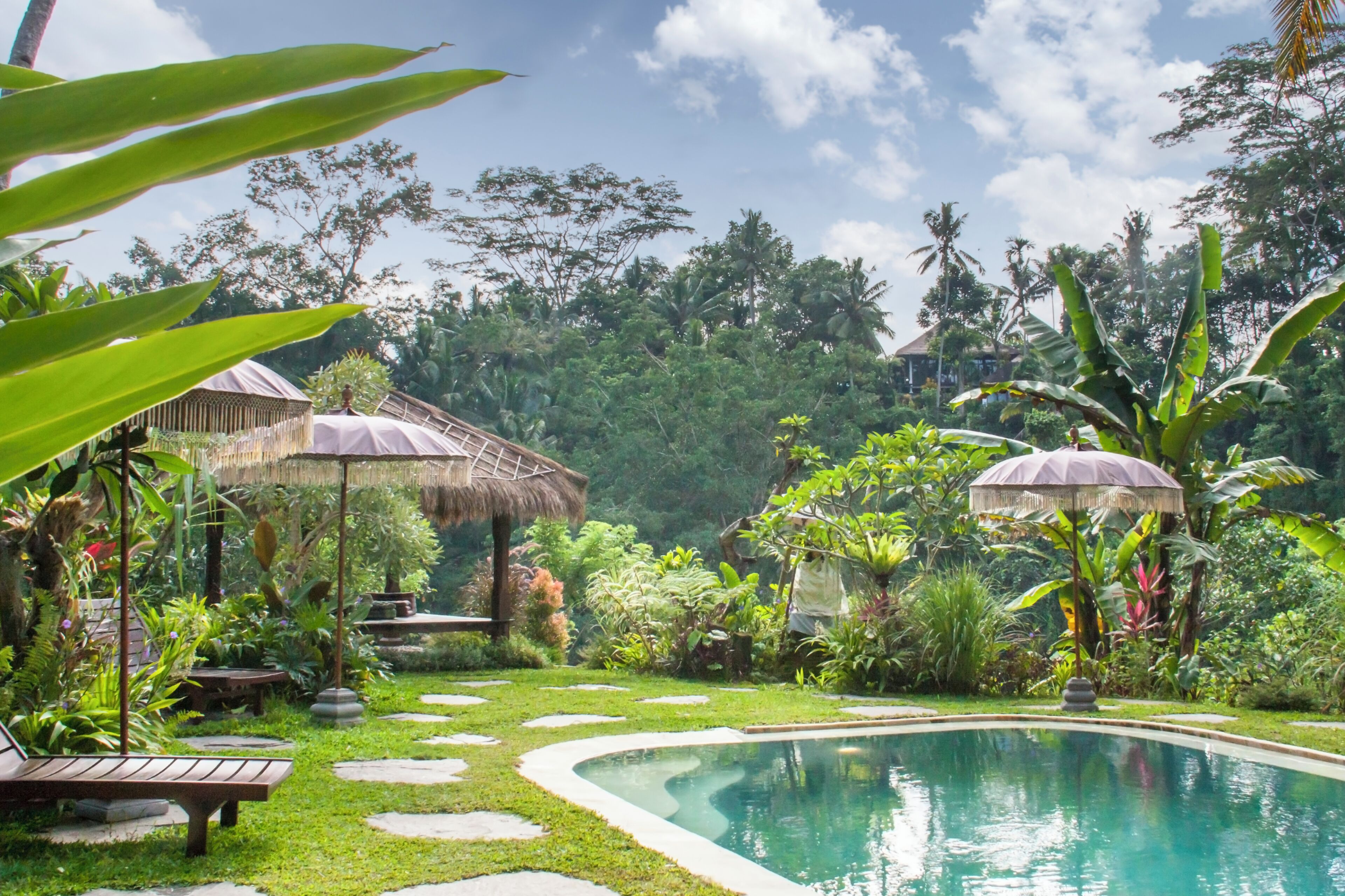 Un jardin tropical doté d’une piscine, de sentiers en pierre et de constructions à toits de chaume.
