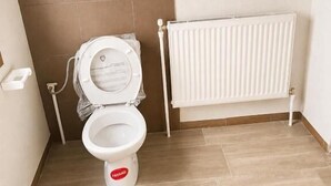 Un baño con inodoro blanco, radiador y piso de baldosas.