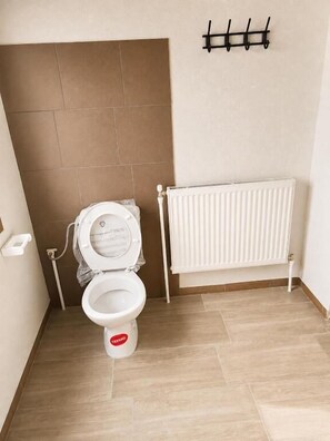 Un baño con inodoro blanco, radiador y piso de baldosas.