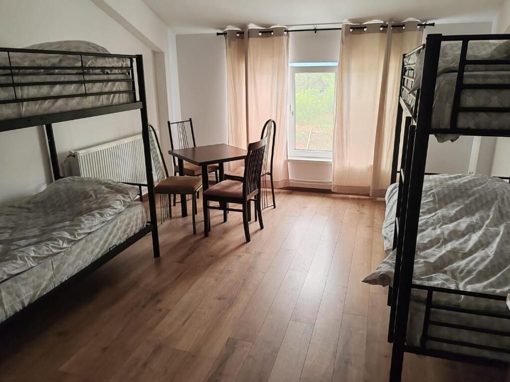 Ein Schlafsaalzimmer mit Etagenbetten, einem Tisch, Stühlen und einem Fenster mit Vorhängen.