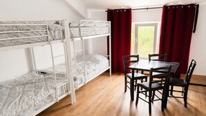 Una habitación con una litera, una mesa de comedor con sillas y una ventana con cortinas.