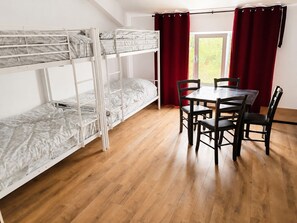 Una habitación con una litera, una mesa de comedor con sillas y una ventana con cortinas.