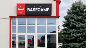 Un hostal llamado BASECAMP con fachada roja y blanca, amplias ventanas y un estacionamiento visible.