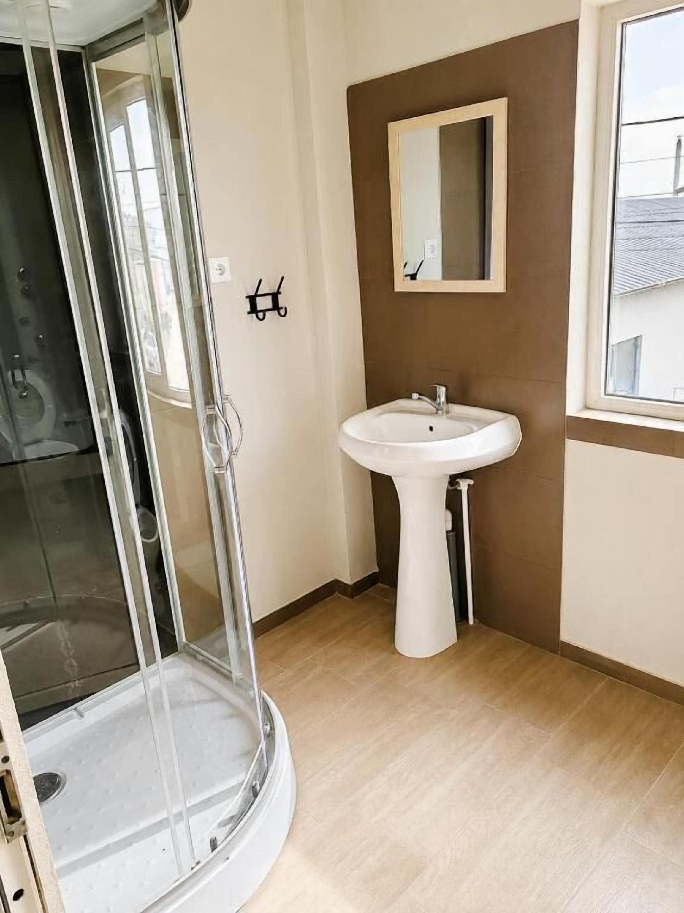 Une salle de bain avec une douche à parois de verre, un lavabo sur colonne et un miroir au mur.