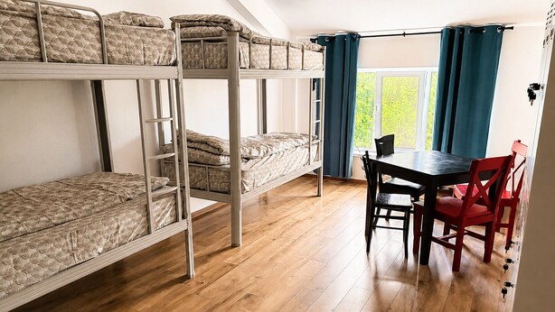 Un dormitorio con literas, piso de madera, una mesa con sillas y una ventana con cortinas.