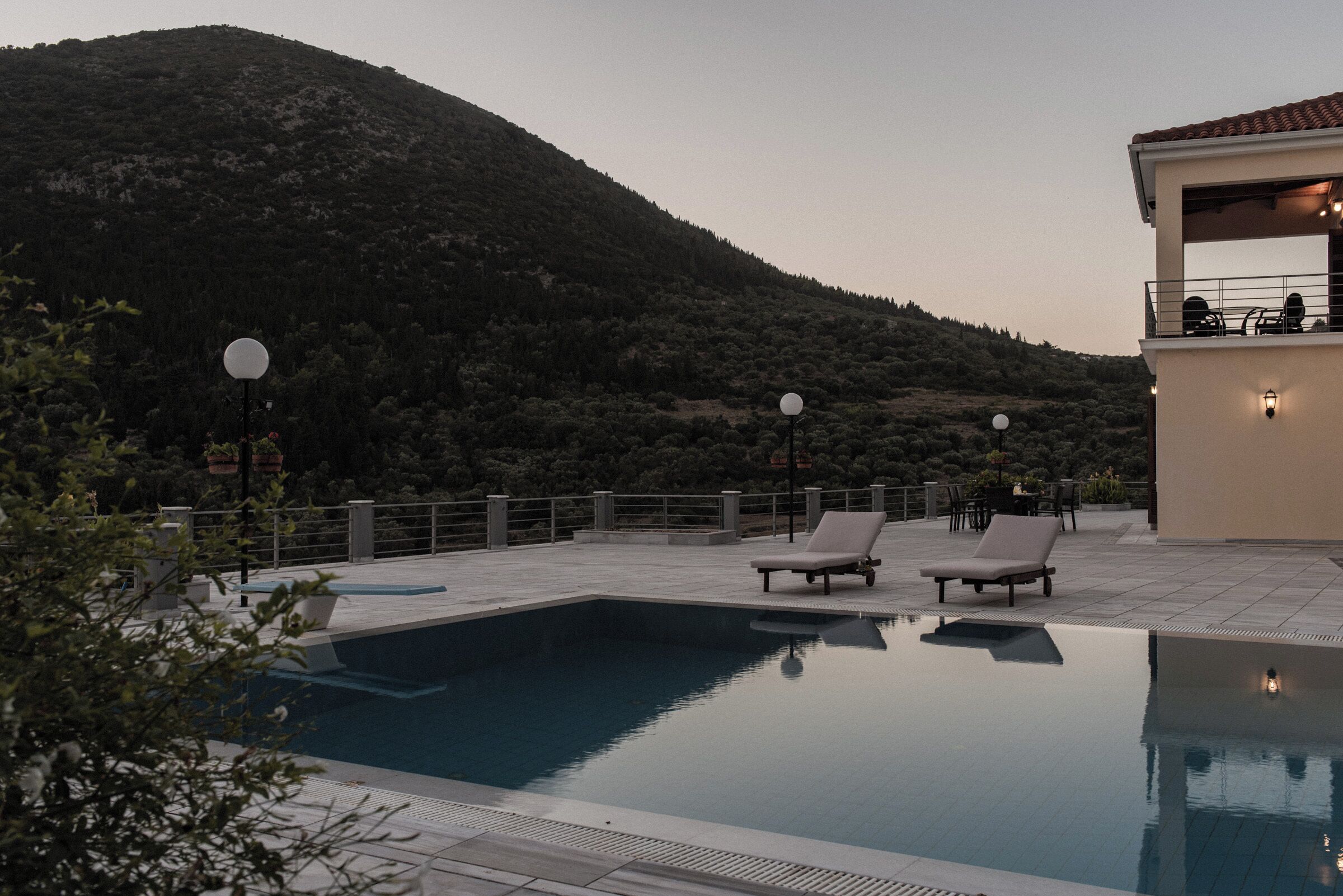 Ein Pool mit Liegestühlen, im Hintergrund Berge und ein Gebäude mit Außenbereich.