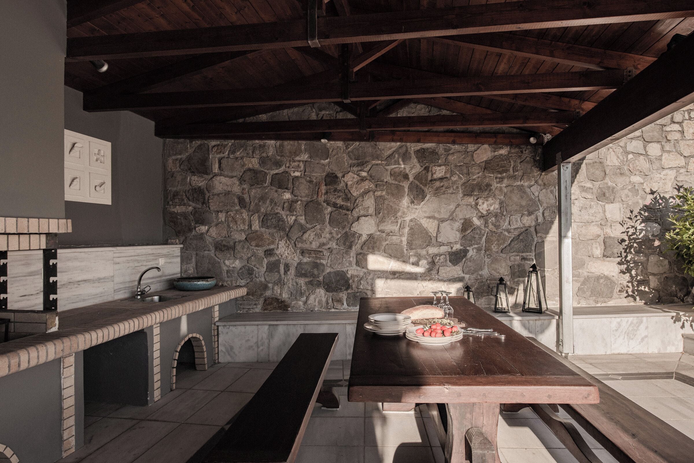 Une cuisine extérieure rustique, avec un mur en pierre en arrière-plan, une table en bois et un banc.