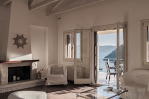 A spacious living room with a fireplace, a comfortable seating area, and a view of the sea. - Villa Idylle | Ithaca Greece (Ithaki)